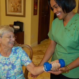 A healthcare worker assists a senior woman with physical therapy exercises.