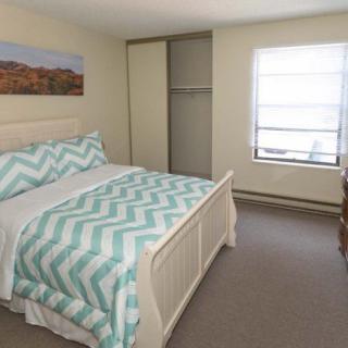 A cozy bedroom with a neatly made bed featuring a zigzag patterned duvet, a window allowing natural light, and an open closet.