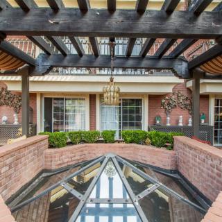 A charming courtyard with a wooden pergola and glass roof, surrounded by brick walls and adorned with a chandelier.