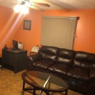 A cozy living room with an orange accent wall, featuring a leather sofa and a glass coffee table.
