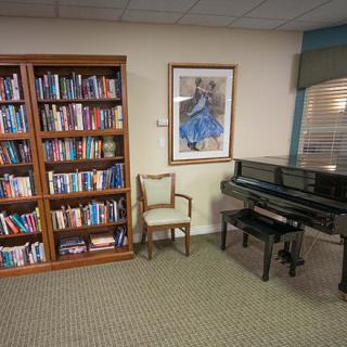 A cozy library corner with a bookshelf, piano, and chair.