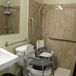 An accessible bathroom equipped with grab bars, a shower chair, and toilet aids.