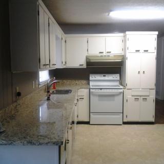 A kitchen with white cabinets and appliances, featuring a marble countertop.