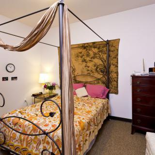 A cozy bedroom featuring a canopy bed with ornate metalwork, complemented by a tapestry and warm lighting.