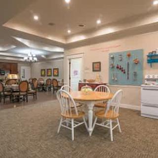 A cozy dining and kitchen area with ambient lighting, featuring a central table and chairs surrounded by decorative elements.