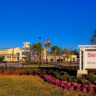 A well-maintained building surrounded by palm trees and vibrant flowers under a clear blue sky.