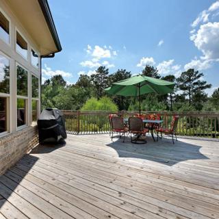 A spacious wooden deck with a table, chairs, and an umbrella, surrounded by nature on a sunny day.