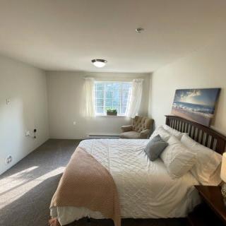A minimalist bedroom with a bed, chair, and window letting in natural light.