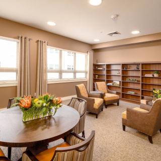 A cozy, well-lit living room with comfortable chairs, a round table, and bookshelves.