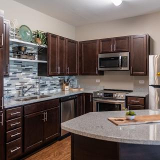 A modern kitchen featuring dark cabinetry, stainless steel appliances, and a central island with a granite countertop.