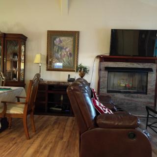 A cozy living room featuring a leather chair, a fireplace, and a television, adjacent to a dining area with elegant furniture and artwork on the wall.
