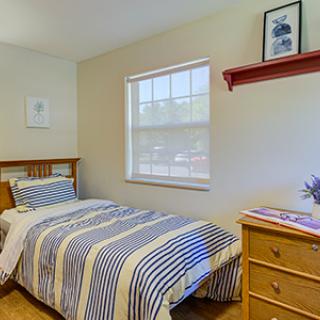 A cozy bedroom featuring a single bed with striped bedding, a small window, and minimalist decor.