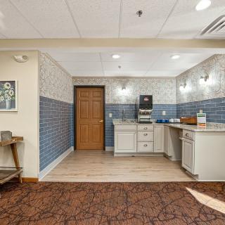 A kitchenette area featuring a coffee station, cabinets, and distinct tile and carpet flooring.