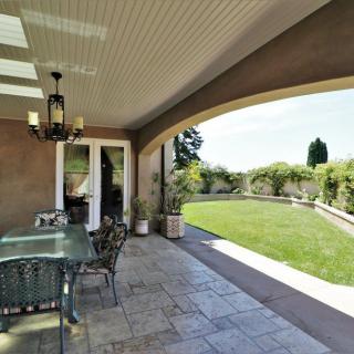 A covered patio with outdoor furniture overlooking a well-maintained lawn and garden.