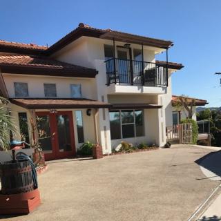 A modern two-story house with a red tile roof and spacious driveway under a clear blue sky.