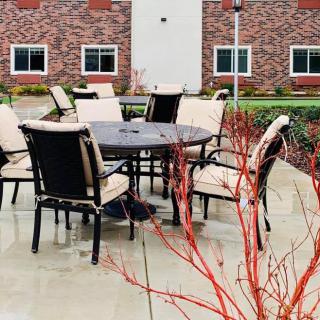 An outdoor patio setting with chairs and a table, situated near a brick building on a rainy day.