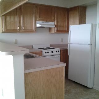A small apartment kitchen with wood cabinets, a refrigerator, and a stove.