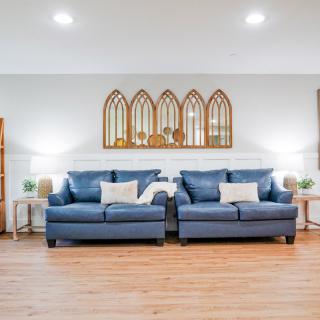 A modern living room featuring two blue sofas, wooden flooring, and decorative mirror art on the wall.
