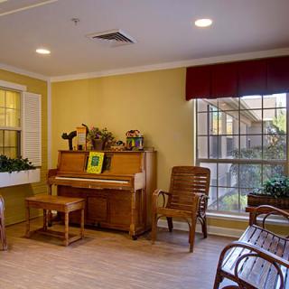 A cozy living room with a piano, chairs, and large windows.