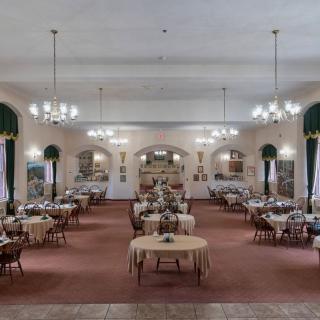 A spacious dining hall with chandeliers and neatly arranged tables.