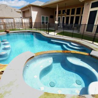 A backyard with a swimming pool and adjacent hot tub surrounded by a safety fence.