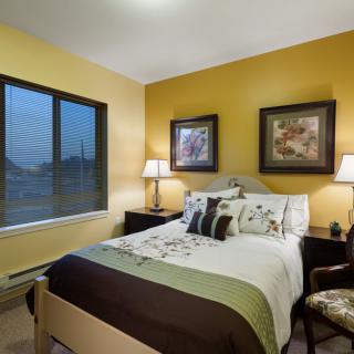 A cozy bedroom with warm yellow walls, featuring a neatly made bed and elegant decor.