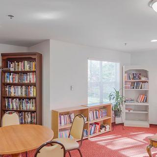 A cozy library room with bookshelves, tables, and chairs next to a window.