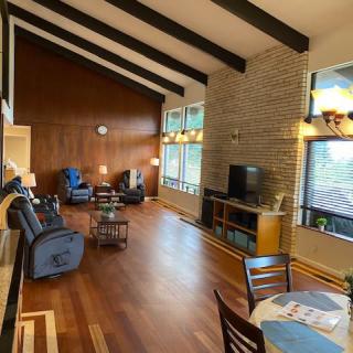 A spacious mid-century modern living room featuring wood paneling, exposed beams, and large windows.