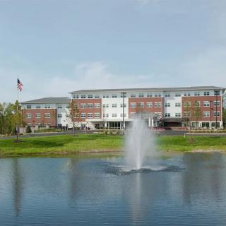 A building with a fountain in front, set beside a pond and surrounded by greenery.