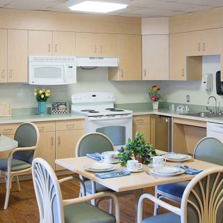 A modern kitchen and dining area featuring light wooden cabinets, a white stove and microwave, and a neatly set table with chairs.