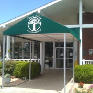 The entrance of a building featuring a green canopy and well-maintained landscaping.