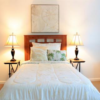 A cozy bedroom with a neatly made bed, flanked by side tables and lamps, featuring simple decor.