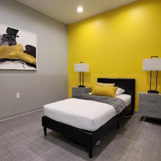 A modern bedroom featuring a yellow accent wall, sleek furniture, and contemporary artwork.