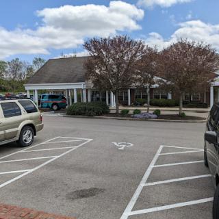 A serene view of a parking lot with a building, trees, and a cloudy sky.