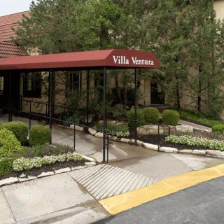 Entrance to a villa with a red awning and landscaped surroundings.