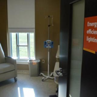 A hospital room featuring an IV stand next to a chair and a window, with an energy efficiency sign on the wall.