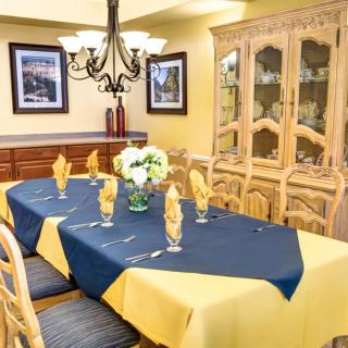 A beautifully set dining room table with blue and yellow linens, surrounded by elegant wooden chairs.
