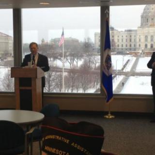 A speaker giving a speech indoors with a snowy landscape visible through the window.