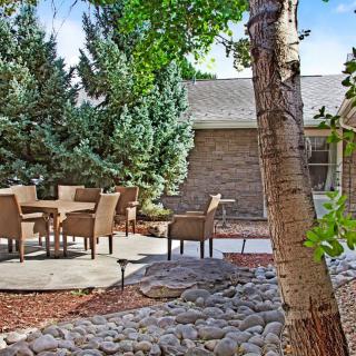 A peaceful backyard patio with outdoor seating surrounded by trees and a rocky garden.