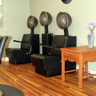Three hair dryer chairs lined up in a salon with wooden flooring.
