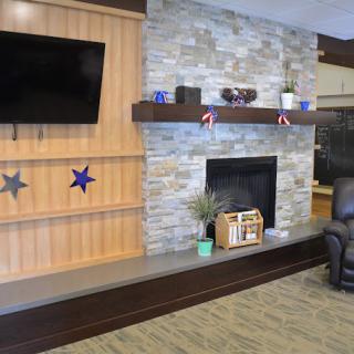 A modern living room with a stone fireplace, wall-mounted television, and decorative shelving.