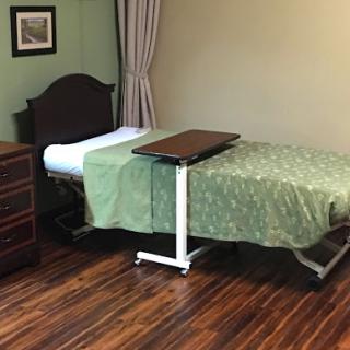 A simple hospital room featuring a medical bed with green bedding and a wooden dresser.