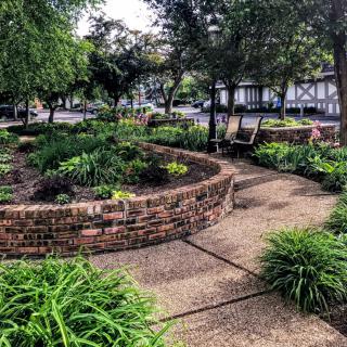 A beautifully landscaped garden featuring a circular brick wall, lush greenery, and a winding pathway.
