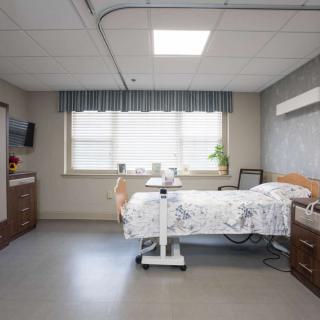 A clean and well-organized hospital room with a single bed, window, and medical equipment.