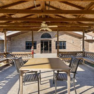 A spacious outdoor patio area featuring a wooden roof, a table with chairs, and a ceiling fan, providing a comfortable space to relax.