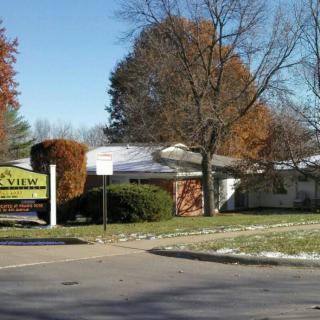 A real estate office surrounded by autumn trees with a sign in front.