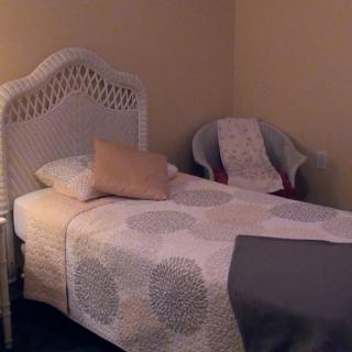 A cozy bedroom with a single bed featuring a wicker headboard and adjacent chair.