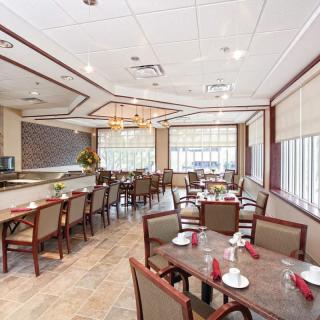 A well-lit restaurant dining area with neatly arranged tables and chairs, featuring a chandelier and large windows.