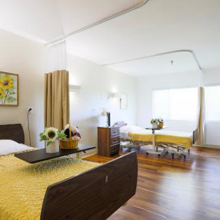A spacious and well-lit hospital room featuring two beds, modern furnishings, and decorative elements.