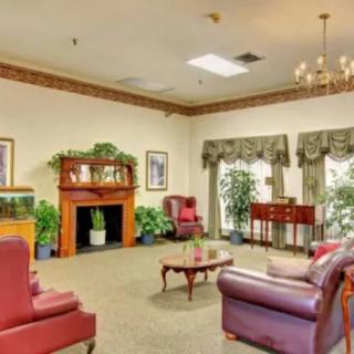 A cozy living room with traditional decor, featuring comfortable seating, a fireplace, and lush plants.